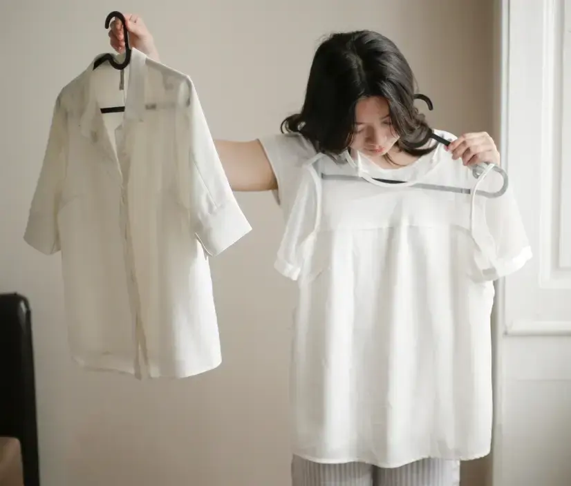 Woman comparing white garments on hangers in a minimalist studio