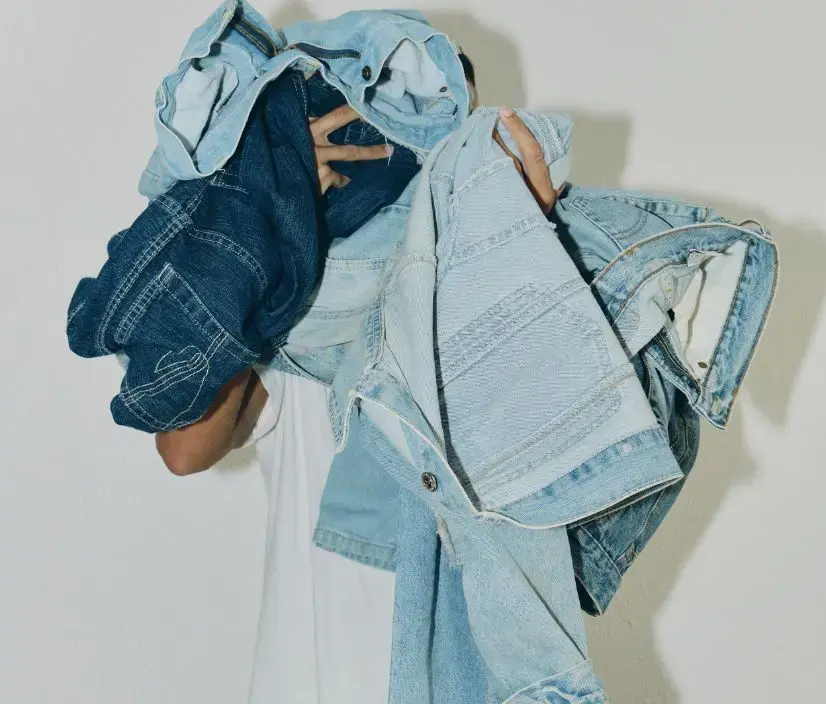 Person holding an armful of light and dark denim jeans and jackets