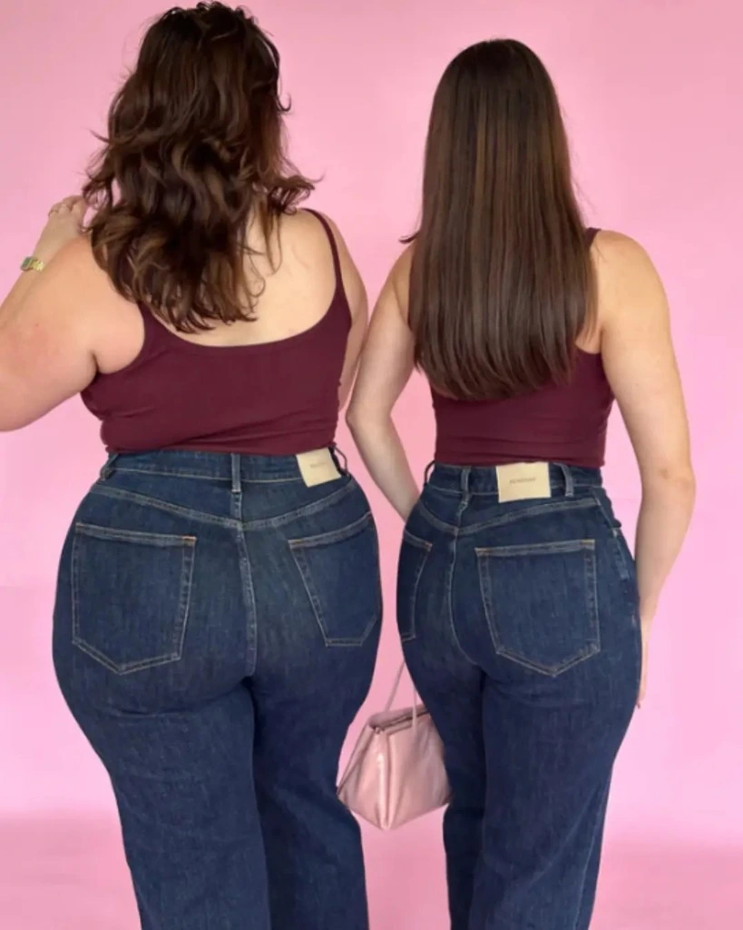 Two Peachay models in matching dark-wash high-waisted jeans against a pink backdrop, showing a flush waist fit from behind